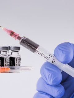 Featured nurse hand holding syringe with medical vials in background