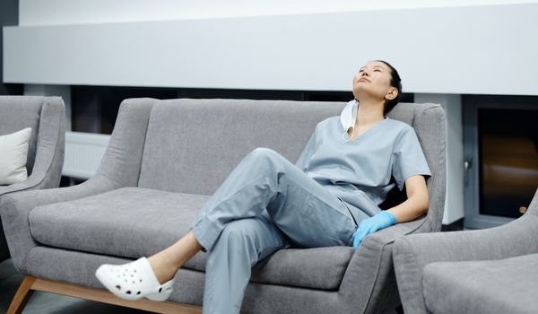 lady nurse in scrubs tired sitting on couch at hospital lobby