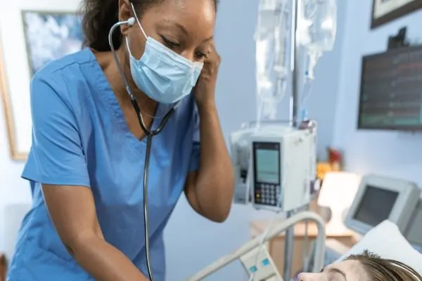 nurse listening to lung sounds with stethoscope on a woman laying on hospital bed