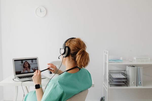 nurse working from home talking to a patient on laptop with headset on 