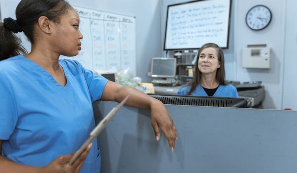one nurse asking another nurse for help at nursing station 