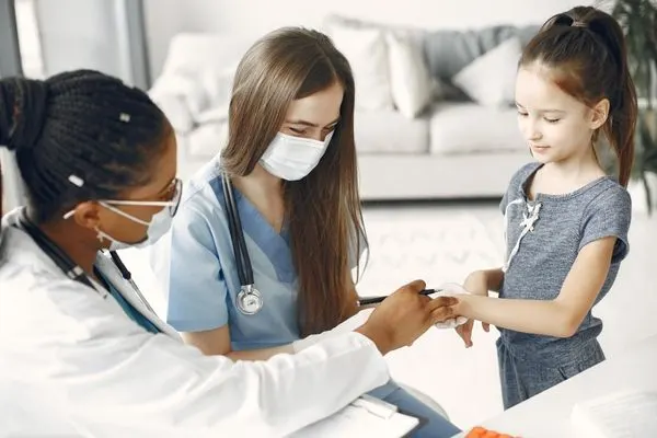 school nurse and doctor wearing stethoscope and mask assessing a young girl in an office