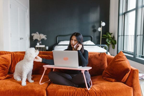 women on phone sitting on couch and petting her dog next to her