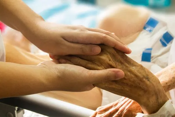 young woman's hand holding older patient's hand 