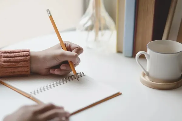 student in nursing program writing on notebook with pencil with a mug on a desk