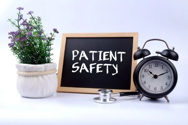 A image with a plant pot , a clock and a black board with Patient Safety mentioned on it.