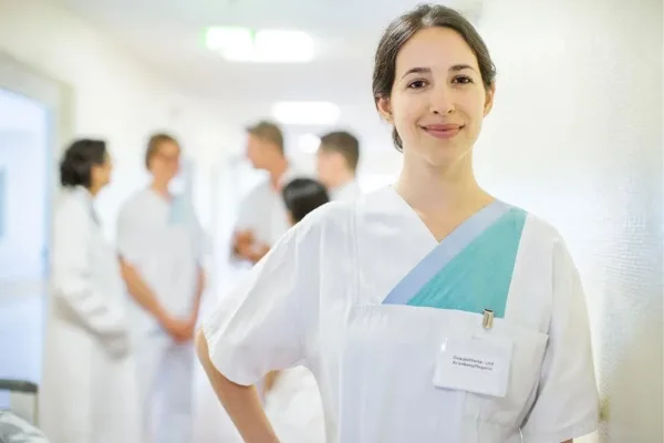 Nurse wearing a badge while a group of medical staff in the background talking to each other at a hospital hallway
