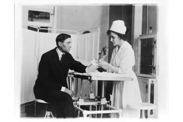 An old image of a nurse wearing a traditional nurse attire with a nurse hat taking a patients blood sample